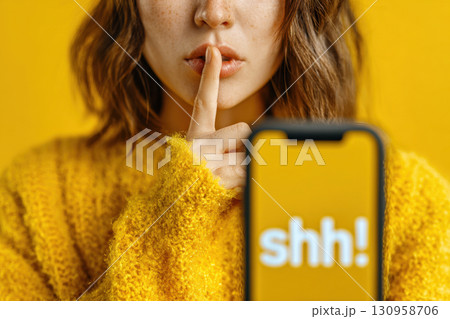 Woman showing silence gesture with smartphone on yellow background 130958706