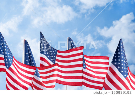 Waving United States flags on bright sky backdrop, symbol of liberty and democracy. Background for Memorial Day posters, Veterans Day banners, and patriotic holiday designs. Waving United States flags on bright sky backdrop, symbol of liberty and democracy. Background for Memorial Day posters, Veterans Day banners, and patriotic holiday designs. 130959192
