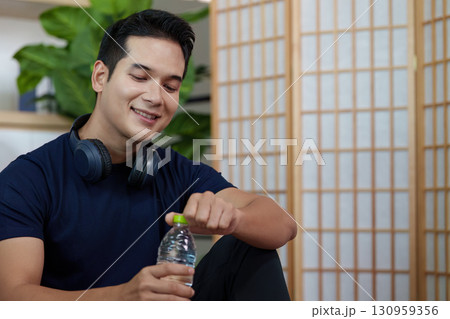 Healthy Lifestyle. Young man enjoying hydration with water bottle and headphones. 130959356