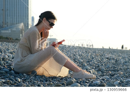 Thoughtful woman browse smartphone sits on pebble coast in Batumi city Georgia. Thoughtful woman browse smartphone sits on pebble coast in Batumi city Georgia. 130959666