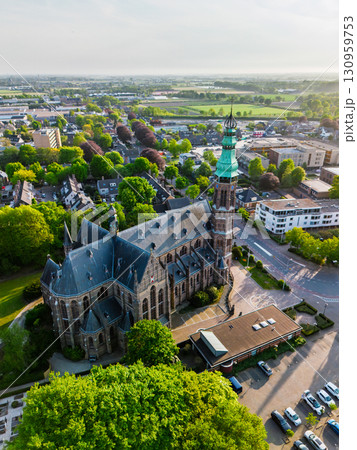 A European town with a tall green-spired Gothic church at its center, surrounded by houses, trees, and streets, glowing warmly in golden hour light. 130959753