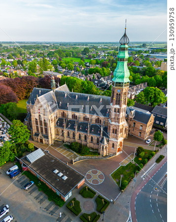 A Gothic-style church with a tall green spire and ornate bell tower stands amid gardens, paths, and nearby houses, blending historic elegance with a suburban setting. 130959758