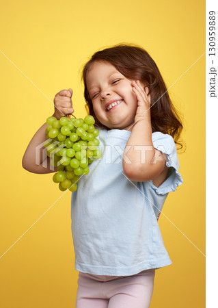 smiling Caucasian little child girl holding bunch of green grapes on yellow background smiling Caucasian little child girl holding bunch of green grapes on yellow background 130959889