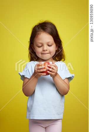Portrait of brunette little child girl with peach on yellow background Portrait of brunette little child girl with peach on yellow background 130959890