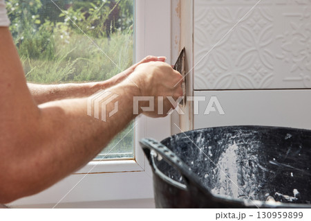 Caucasian plasterer man with a spatula applying finishing putty on a window opening Caucasian plasterer man with a spatula applying finishing putty on a window opening 130959899