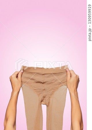 female hands holding beige nylon pantyhose on pink background. female hands holding beige nylon pantyhose on pink background. 130959919