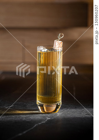 Highball cocktail with ice cube and golden glow Highball cocktail with ice cube and golden glow 130960207