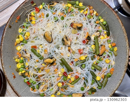 This bright and colorful dish consisting of rice noodles, fresh vegetables and juicy mussels in a pan in a home kitchen is ideal for healthy eating. Close-up. 130962303