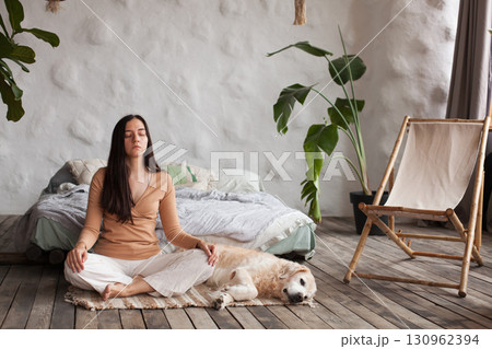 Mindful woman practices yoga at home with her golden retriever in a calming space 130962394