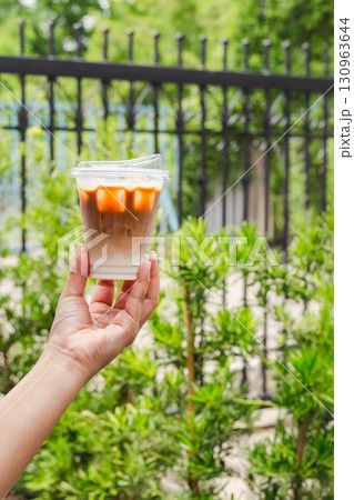 Woman hand holding iced coffee on a nature background. Woman hand holding iced coffee on a nature background. 130963644