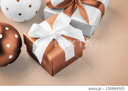 Brown gift box with white bow ribbon and xmas ball on light brown background, closeup 130964301