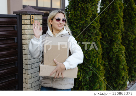 Delivery woman waving while holding cardboard boxes and wearing sunglasses Delivery woman waving while holding cardboard boxes and wearing sunglasses 130965375