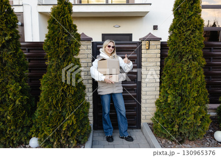 Courier holding parcel and showing thumb up in front of house Courier holding parcel and showing thumb up in front of house 130965376