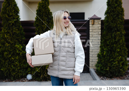 Delivery woman carrying cardboard boxes in front of a house 130965390
