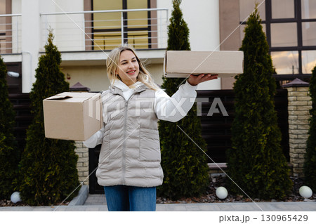 Delivery woman holding two cardboard boxes in front of a house Delivery woman holding two cardboard boxes in front of a house 130965429