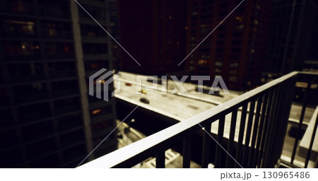 A balcony railing frames a vibrant city street at night, illuminated by the glow of lights from buildings. Cars move along the roadway, enhancing the urban atmosphere. A balcony railing frames a vibrant city street at night, illuminated by the glow of lights from buildings. Cars move along the roadway, enhancing the urban atmosphere. 130965486