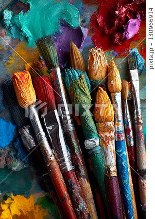 A collection of various paintbrushes dipped in vivid acrylic colors on an artist's messy palette, ready for creation. 130966914