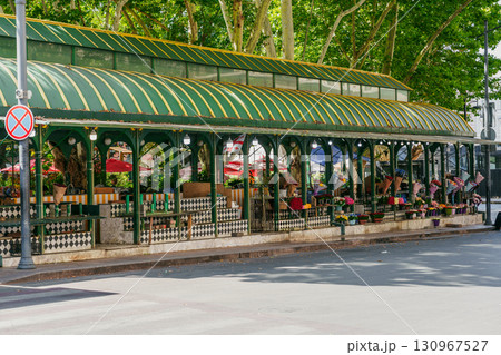 Green awning shelter in a city park with colorful flower displays and outdoor seating on a sunny day Green awning shelter in a city park with colorful flower displays and outdoor seating on a sunny day 130967527