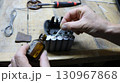 Processing contacts on old batteries from a construction tool during device resuscitation, close-up of male hands applying solution from a brown glass bottle to battery contacts on a work table 130967868