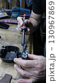 A repairman's hands with a small soldering iron while restoring a screwdriver battery, working with a hand soldering iron on a workbench surface while repairing a screwdriver battery 130967869