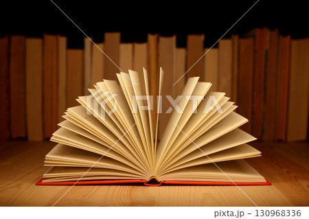 Old open book on wooden table near row of many old and new books. Concept of knowledge, information. Old open book on wooden table near row of many old and new books. Concept of knowledge, information. 130968336