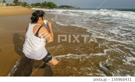 A middle-aged Asian woman sitting on a rock on a sunset beach in Liberia, West Africa. 130968431