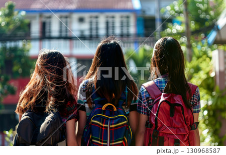 The back view of a little kid wearing bright and colorful backpacks while walking into the primary or elementary school with other strident. Generative AI. 130968587