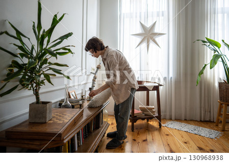 Calm woman reaching over table with cleaning duster tool to wipe surfaces and maintain home hygiene 130968938