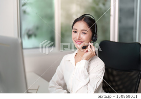 Friendly Call Center Agent Smiling While on Call in Office Friendly Call Center Agent Smiling While on Call in Office 130969011