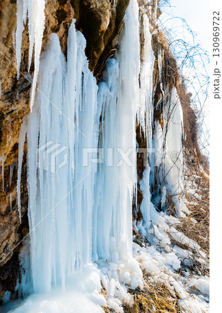 Frozen waterfall with long icicles on a rocky cliff in winter. 130969722