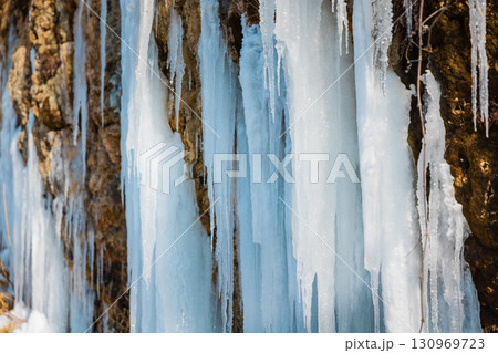 Frozen waterfall with long icicles on a rocky cliff in winter. 130969723