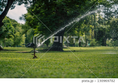 sprinkler watering lush lawn in vibrant garden, irrigation system hydrating green turf with refreshing water spray 130969782