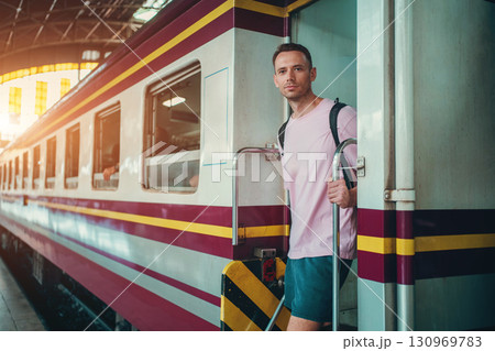 traveler guy boarding train at busy railroad station, young man with backpack starting journey on railway platform traveler guy boarding train at busy railroad station, young man with backpack starting journey on railway platform 130969783