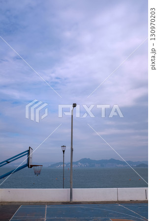 The scene of outdoor basketball court with seascape and skyscape. Outdoor sports and recreation court. Nobody in the basketball court in the sunny day. Sports and recreation concept. The scene of outdoor basketball court with seascape and skyscape. Outdoor sports and recreation court. Nobody in the basketball court in the sunny day. Sports and recreation concept. 130970203