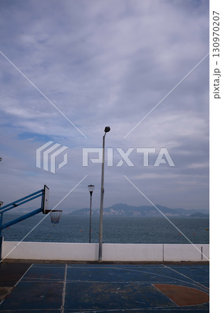 The scene of outdoor basketball court with seascape and skyscape. Outdoor sports and recreation court. Nobody in the basketball court in the sunny day. Sports and recreation concept. 130970207