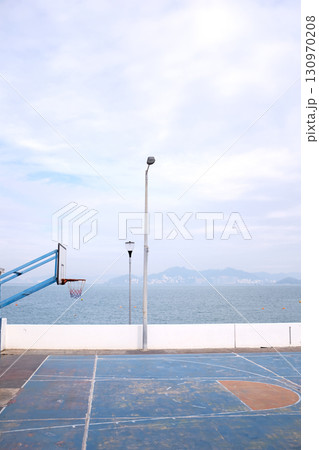 The scene of outdoor basketball court with seascape and skyscape. Outdoor sports and recreation court. Nobody in the basketball court in the sunny day. Sports and recreation concept. 130970208