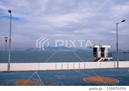 The scene of outdoor basketball court with seascape and skyscape. Outdoor sports and recreation court. Nobody in the basketball court in the sunny day. Sports and recreation concept. 130970209