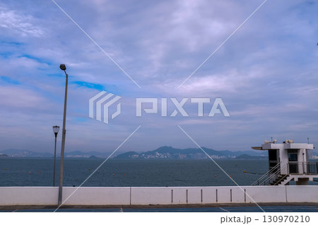 The scene of outdoor basketball court with seascape and skyscape. Outdoor sports and recreation court. Nobody in the basketball court in the sunny day. Sports and recreation concept. 130970210