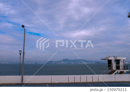 The scene of outdoor basketball court with seascape and skyscape. Outdoor sports and recreation court. Nobody in the basketball court in the sunny day. Sports and recreation concept. 130970211
