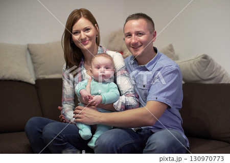 Young couple sitting on couch with his 3 months old baby boy, posing for family photo Young couple sitting on couch with his 3 months old baby boy, posing for family photo 130970773