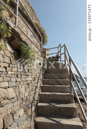 Stone path with iron railings leading to sea on sunny summer day. Nature and buildings. 130971475