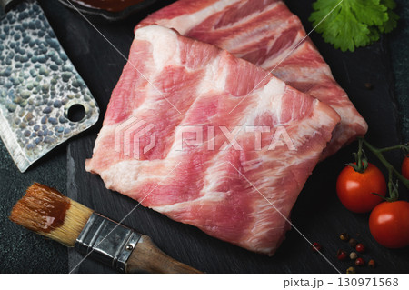 Raw meat. Raw pork ribs from the back with meat on a black background. background image Raw meat. Raw pork ribs from the back with meat on a black background. background image 130971568