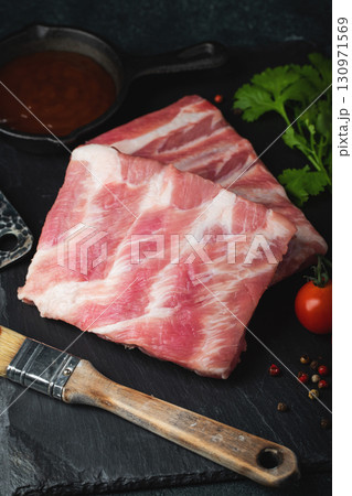 Raw meat. Raw pork ribs from the back with meat on a black background. background image Raw meat. Raw pork ribs from the back with meat on a black background. background image 130971569