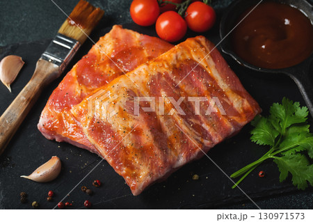 Ready for BBQ raw pork spare ribs with barbecue sauce. Black background. Top view Ready for BBQ raw pork spare ribs with barbecue sauce. Black background. Top view 130971573