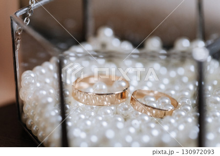 Golden wedding rings in glass box filled with white pearls, symbol of love and unity Golden wedding rings in glass box filled with white pearls, symbol of love and unity 130972093