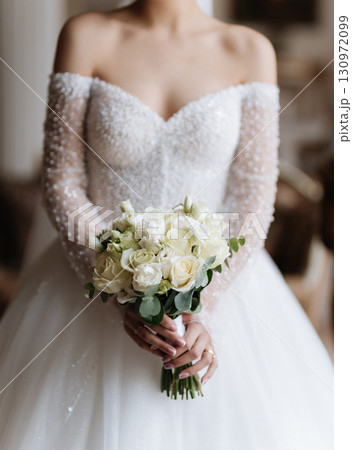 Elegant bride holding bouquet of white roses on wedding day in classic interior Elegant bride holding bouquet of white roses on wedding day in classic interior 130972099