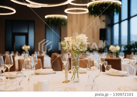 Elegant wedding table setup with white flowers and modern lighting in luxury restaurant 130972101