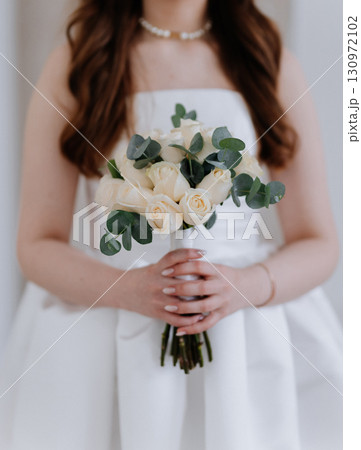 Bride holding elegant bouquet of white roses and eucalyptus in minimalist style 130972102