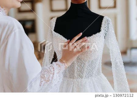 Elegant bride touching luxury pearl wedding dress on mannequin in bridal boutique 130972112
