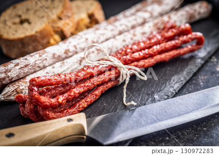 Fuet sausage with mold and smoked kabanos mini salami on black cutting board. 130972283